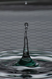 Close-up of drop splashing in water with chess pattern on the background