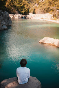 Rear view of woman sitting on rock by lake