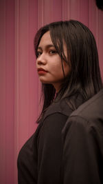 Portrait of young woman looking away against wall