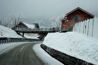 Snow covered road by house against sky during winter