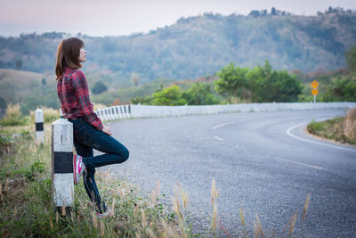 Side view of woman sitting on road against mountain