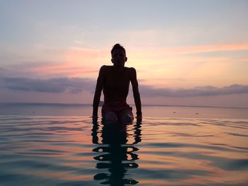 Man on sea against sky during sunset