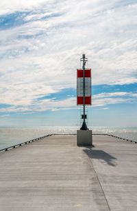 A simple starboard marker and it's long shadow at the end of a cement pier as it juts into the sea