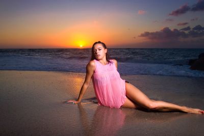 Portrait of sensuous woman sitting on sea shore at beach during sunset