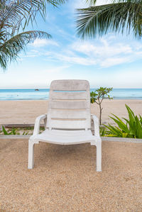 Empty chair on beach by sea against sky