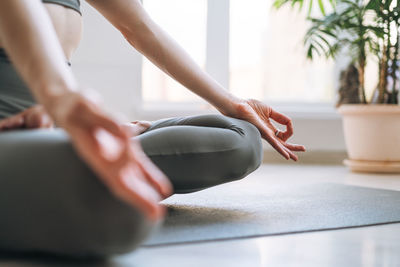 Young fit woman practice yoga doing asana lotus position in light yoga studio with green house plant