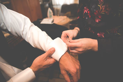 Bride attaching cuff link on bridegroom sleeve during wedding