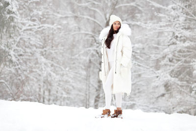 Woman wearing fashionable winter clothes white down jacket, knitted hat, sweater, mittens in  nature