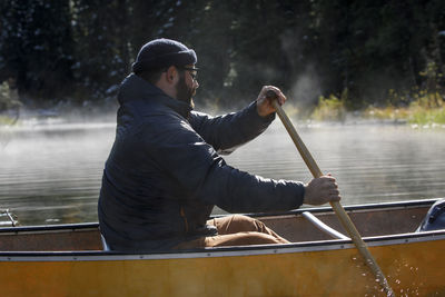 Close up of bearded man paddling canoe on a foggy lake in canada