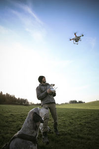 Man on a meadow flying drone while his dog watching