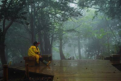 Boy sitting on bench in forest during rainy season