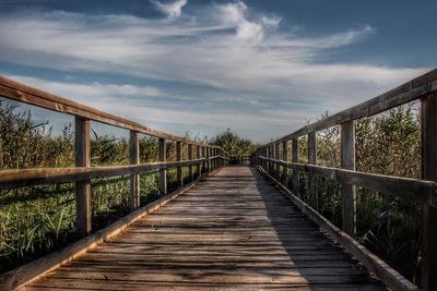 Footbridge leading towards wooden bridge against sky