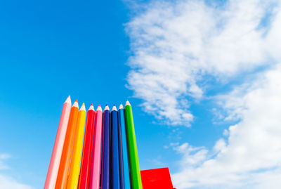 Low angle view of colored pencils against cloudy sky