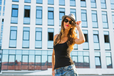 Woman wearing hat standing against built structure