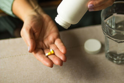 Elderly woman holding white plastic bottle and two capsules in hand, ready to take supplement pills.