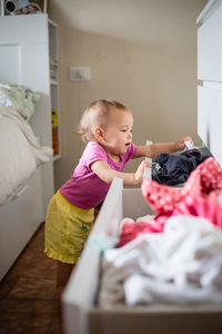 Side view of little baby playing with clothes in the drawers, making order