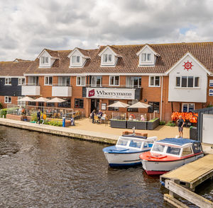 Boats moored on canal by buildings against sky