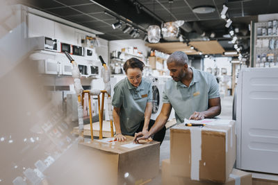 Multiracial male and female colleagues discussing over box while working in electronics store