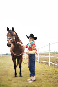 Portrait of smiling girl standing with horse in pen against clear sky