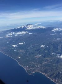 Aerial view of sea and mountains against blue sky