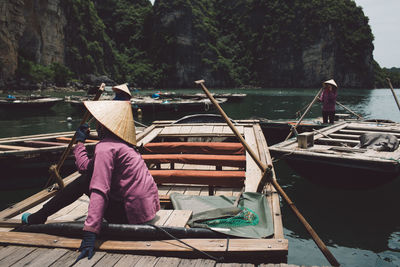 Side view of woman wearing asian style conical hat while sitting on rowboat at halong bay