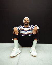 Portrait of young man sitting against black background