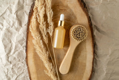 A dropper bottle of serum or oil with vitamin c and a face brush lying on a wooden tray