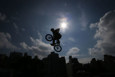 Low angle view of man performing stunt on bicycle by buildings against sky