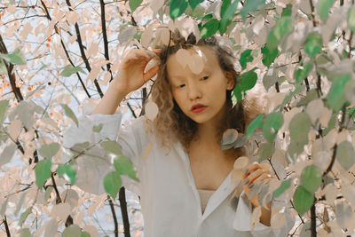 Portrait of woman standing by tree against plants