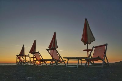 Closed parasols and chairs at beach against clear sky during sunset