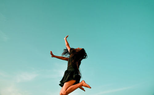 Woman jumping with arms raised against sky