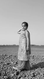 Girl in traditional clothing standing at beach against clear sky