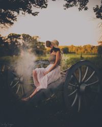 Full length of young woman sitting on cart at farm against sky