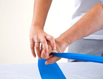 Midsection of woman assisting female in stretching belt against white background