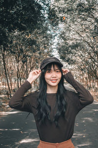 Portrait of smiling young woman standing against trees