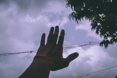 Cropped hand against cloudy sky