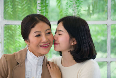 Loving daughter kissing mother against window