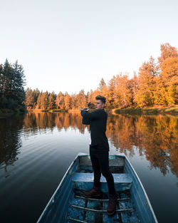 Rear view of man standing by lake against clear sky