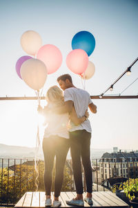 Rear view of couple standing with balloons against sky