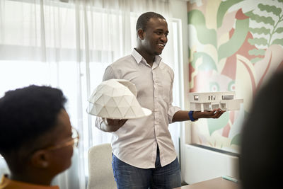 Smiling male architect explaining architectural models during meeting at coworking office