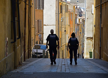 Rear view of police force walking on street amidst buildings