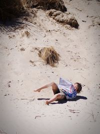 High angle view of little boy lying at beach on sunny day