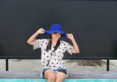 Young woman sitting on retaining wall against billboard