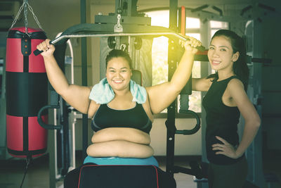Happy young woman exercising with trainer at gym