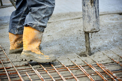 Low section of worker standing on iron rods at construction site