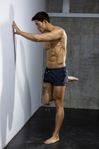 Shirtless muscular man exercising against wall