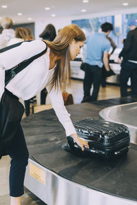 Young businesswoman picking luggage from conveyor belt at airport