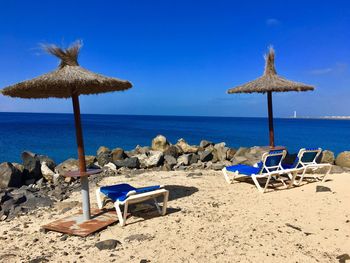 Deck chairs on beach against blue sky