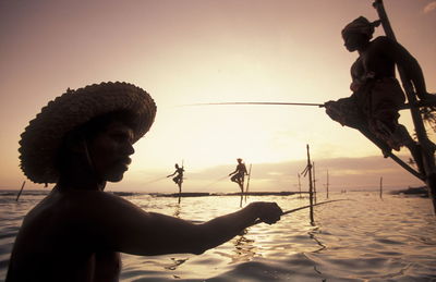 Fishermen fishing over sea against sky during sunset