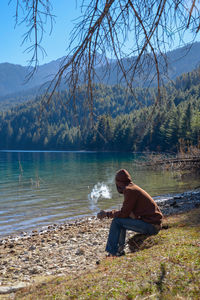 Side view of man sitting at lakeshore in forest